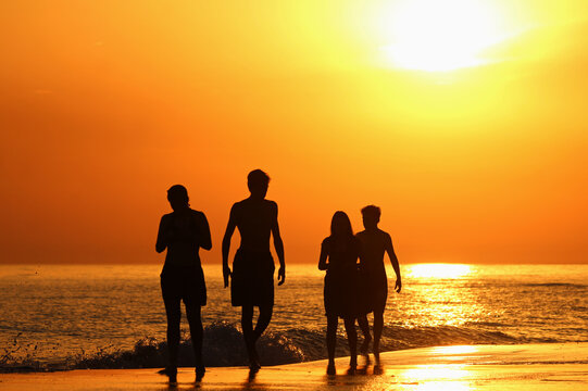 F&aacute;mila feliz contemplando o por do sol, nas f&eacute;rias de ver&atilde;o. Siluetas escuras em fundo laranja ao ar livre. Entardecer no para&iacute;so. Cores vibrantes e contrastantes.