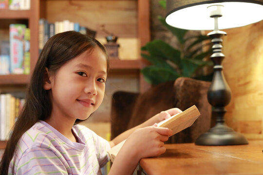 Portrait of Asian girl kid in casual clothes reading a book and smiling on the desk in the room.
