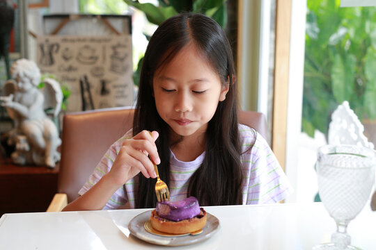 Asian girl child sitting by table and eating Blueberry Cheesecake cake in Cafe. Kid eats tasty food.