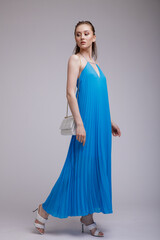 Fototapeta premium High fashion photo of beautiful elegant young woman in a pretty rich blue long dress, handbag, clutch posing over white, soft gray background. Studio Shot, portrait.