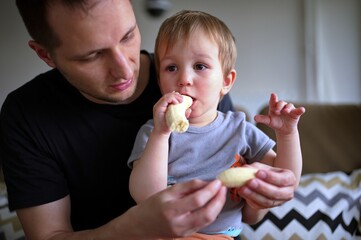 Little toddler eating banana held by his father