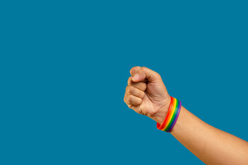 Hand fist with rainbow wristband in a hand while standing against a blue background