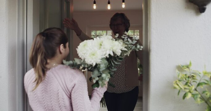 Door, flowers and mothers day surprise with a woman giving her parent a gift at her home during a celebration event. Knock, bouquet and love with an adult daughter surprising her senior mother