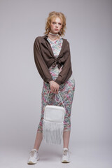 High fashion photo of beautiful elegant young woman in a pretty dress with floral pattern, green brown cardigan, choker, handbag posing over white background. Studio Shot, portrait. Blonde
