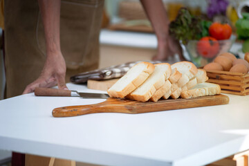 Slices of bread arranged on a wooden tray on a white table While the man standing and rested his hands on the table nearby