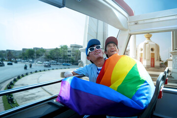 LGBTQ couple with rainbow flag and hugging happily travelers on bus tour at Bangkok Thailand, love and relationship lifestyle concept