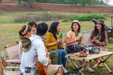 Group of young Asian friends party on vacation enjoy cheering with beer bottle. drinking at camping lake side. hands holding alcoholic beverages. Picnic in holiday.