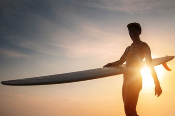 Silhouette surfer woman walks and holding a surfboard as the sunset in the background