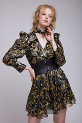 High fashion photo of beautiful elegant young woman in a pretty military camouflage dress with sleeves, boots, wide belt posing over white, soft gray background. Studio Shot, portrait. Blonde