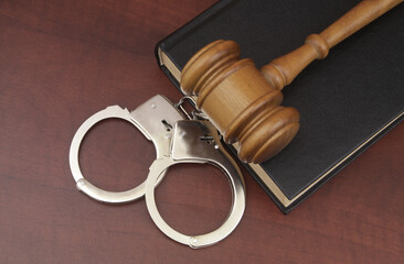 Top view of legal book with wooden gavel and handcuffs on table.