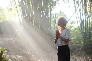 Portrait of a young beautiful girl, blonde, with curly hair, meditating with her hands folded in namaste, in the middle of bamboo trees in the backlight of the visible rays of the morning sun.