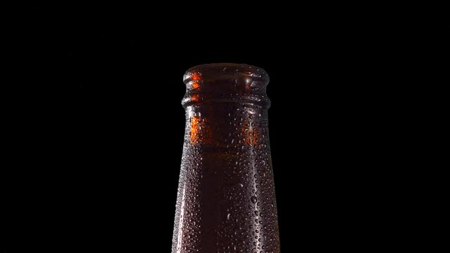 Macro shot Bottleneck Spinning beer bottle ambar glossy wet humid drops detail for background replacement black background