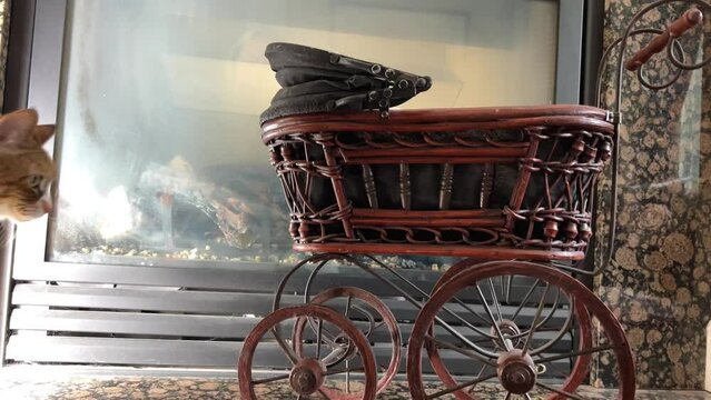 Wicker pram against the background of a fireplace Toy work of art thin wheels like from cart Slightly intimidating Brown wood old red cat 