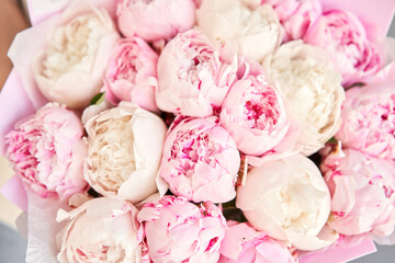 A close-up photo of bouquet of white and pink peonies in women's hands. Flower delivery. A beautiful bouquet of flowers as a gift for a holiday.