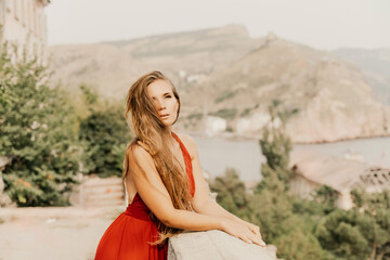 Woman red dress. Summer lifestyle of a happy woman posing near a fence with balusters over the sea.