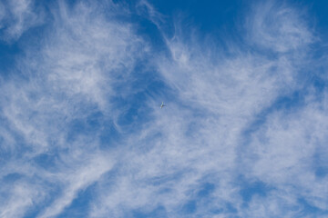 An jetliner flies through wispy wind driven clouds in a blue sky