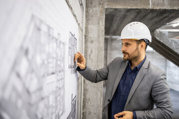Focused caucasian construction engineer checking blueprints and project plan at building site.