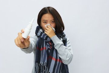 Asian woman flu cold with stuffy nose holds allergy nasal spray with sore throat in plaid scarf on...