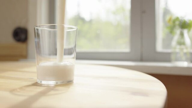 Fermented probiotic milk kefir poured into glass on table, naturally backlit