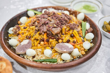 A traditional Uzbek dish called pilaf with meat, carrots, onions, quail eggs and kazy in a plate of astau on the table. A portion for three people. Close up 