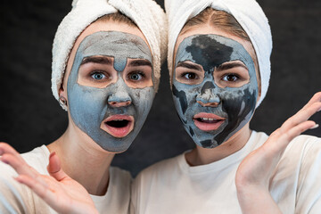 Happy young caucasian sister in hite tshirt towel wearing a charcoal mask on face isolated on black