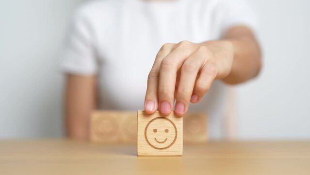 Hand choosing happy face from Emotion block for customer review, good experience, positive feedback, satisfaction, survey, evaluation, assessment, mood and world mental health day concept