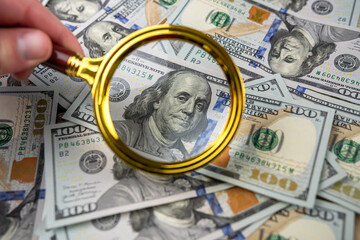 Closeup one hundred US dollar bills under gold magnifying glass