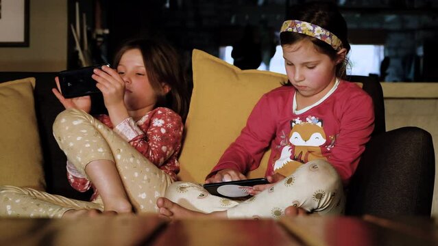 Digital addiction as two sisters play on smartphones on couch, new age kids