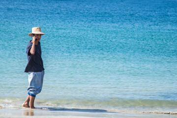 young man walking on the beach and talking on the phone