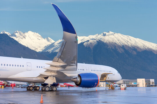 Passenger jet airliner in the parking lot preparing for departure against the backdrop of picturesque snow-capped mountains in the distance.