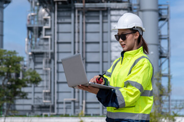 Fototapeta na wymiar Engineer wearing uniform ,helmet and glass stand hand holding tablet computer,radio communication inspection and surveying work site progress with oil refinery power industrial factory background