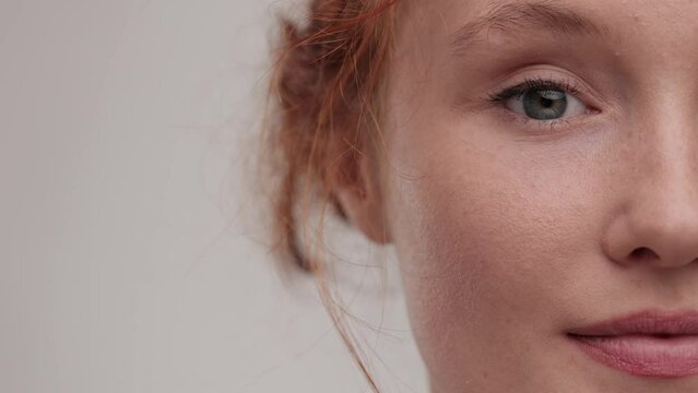 Close up view half face of beautiful young woman. Portrait pretty ginger female with nude make look at the camera in studio background. Concept of cosmetology, skincare.