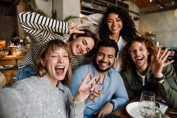 Group of cheerful friends taking selfie while dining in restaurant