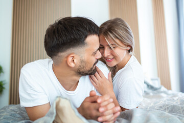 Fototapeta premium smiling couple going to kiss under sleeping sheets in the morning. In love young happy couple lying in bed in the morning