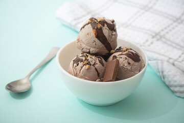 Chocolate ice cream decorated with nuts and chocolate icing, in a white bowl, blue background. Summer homemade cooling desserts