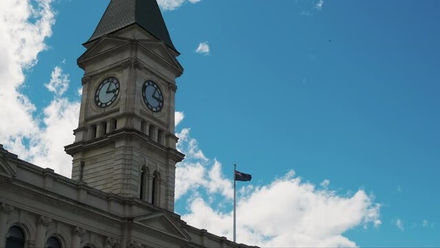 Iconic clock tower of Oamaru, New Zealand, against a blue sky, with the flag proudly waving in the breeze