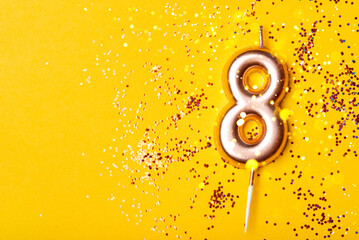 Gold candle in the form of number eight on yellow background with confetti.