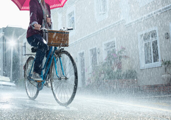 Woman riding bicycle with umbrella in rainy street