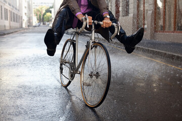 Businessman riding bicycle with feet up in rain