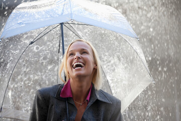 Laughing businesswoman under umbrella in rain