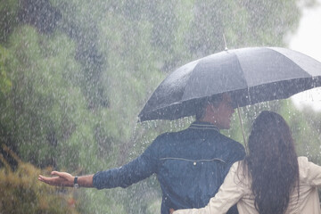 Couple walking with arms outstretched under umbrella in rain