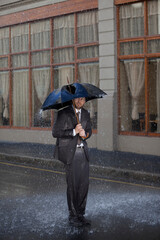 Businessman standing under broken umbrella in rainy street