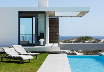 Lounge chairs and lap pool outside modern house overlooking ocean