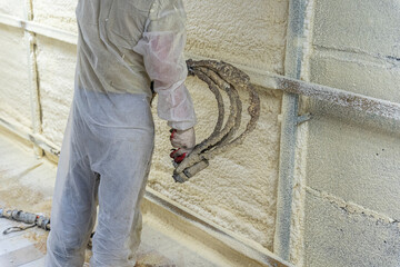 worker in a protective suit insulates the walls with polyurethane foam