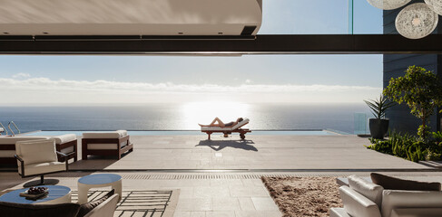 Woman sunbathing on lounge chair at poolside overlooking ocean