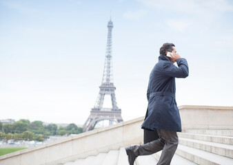 Businessman talking on cell phone ascending steps near Eiffel Tower, Paris, France