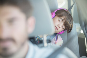 Girl with headphones sleeping in back seat of car