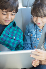 Brother and sister sharing digital tablet in back seat of car