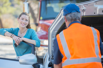 Grateful woman watching roadside mechanic fix car - obrazy, fototapety, plakaty