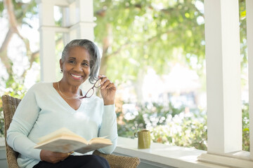 Portrait of smiling senior woman reading book on porch - Powered by Adobe